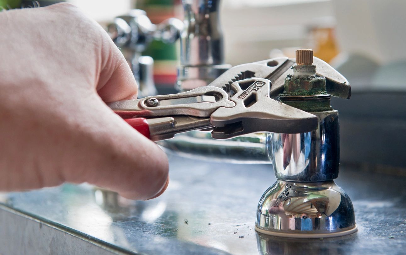 A person is using a pair of pliers to fix the faucet.